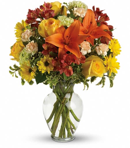 Bouquet of orange lilies, yellow roses, and mixed flowers in a clear glass vase