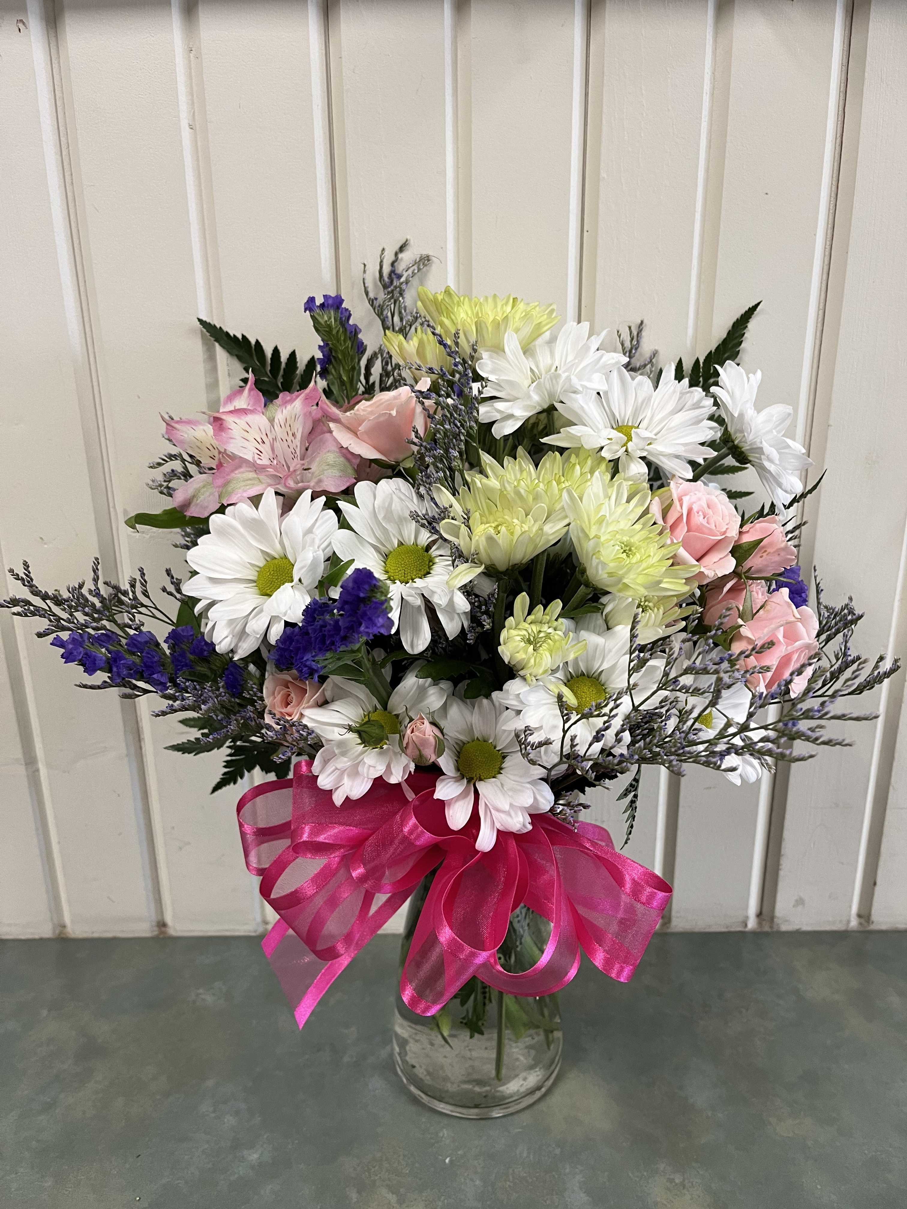 Mixed bouquet of daisies, roses, and alstroemeria in a glass vase with a pink ribbon