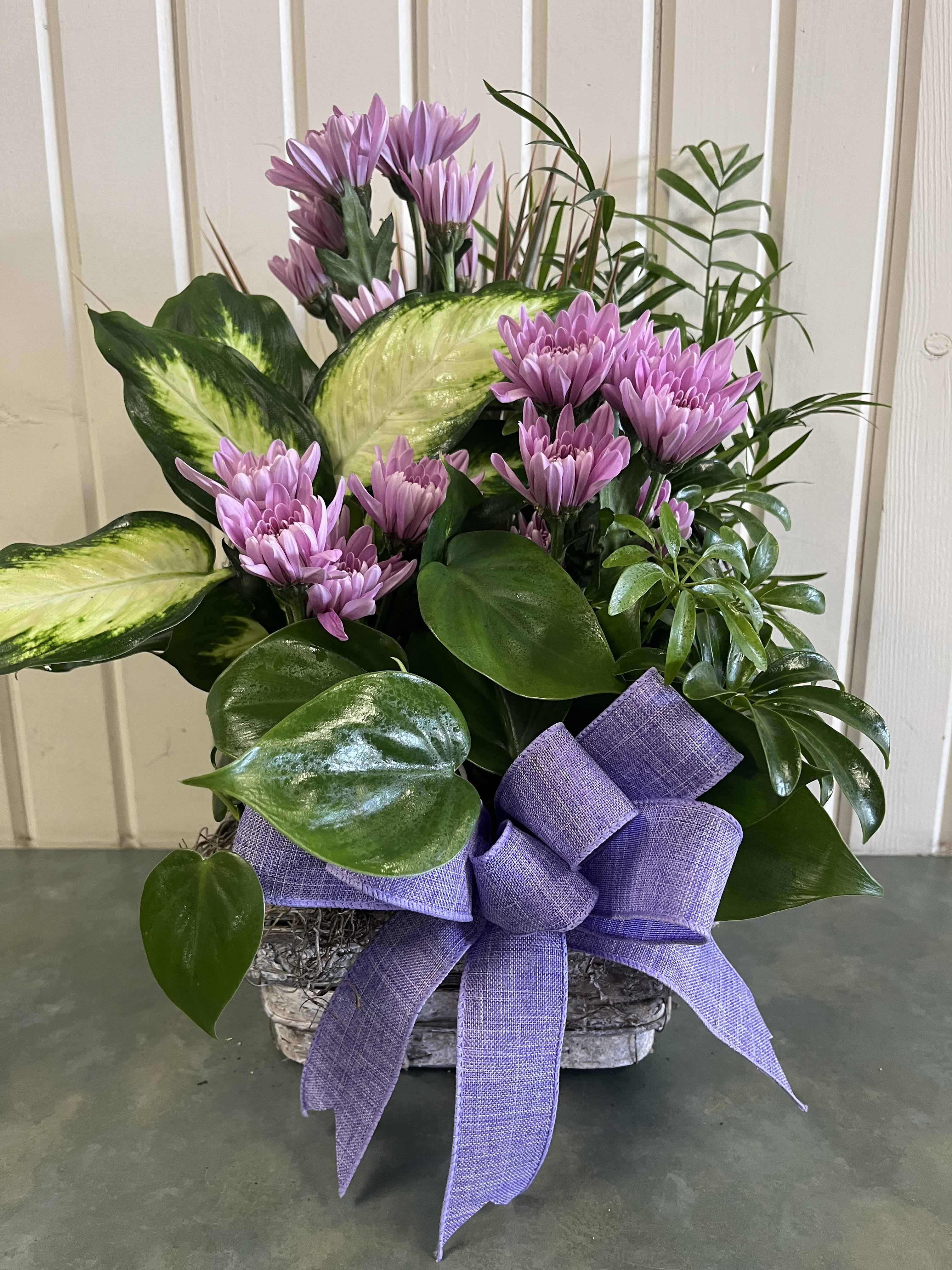 Purple daisy bouquet in a basket with a large lavender bow
