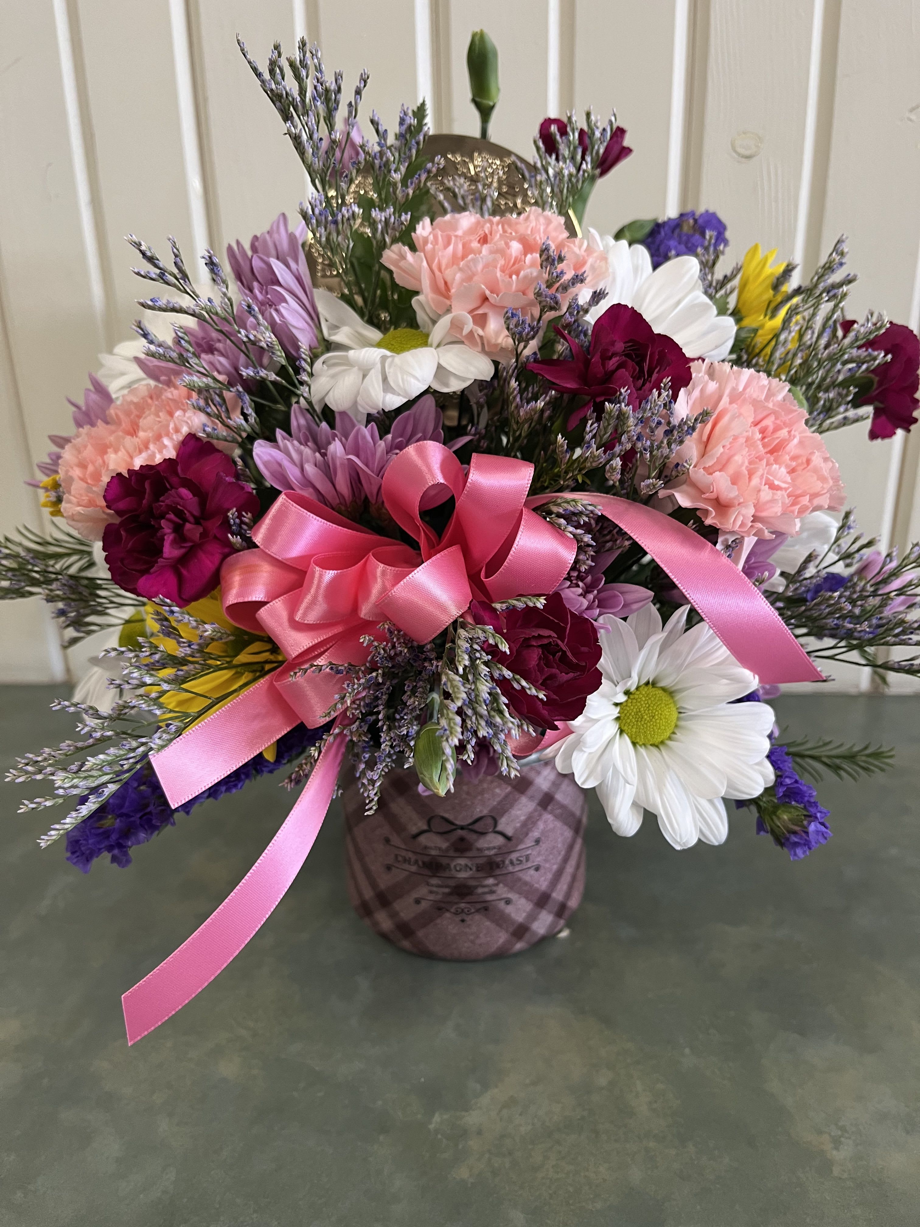 Mixed bouquet of pink, white, and purple flowers in a plaid container with a pink ribbon