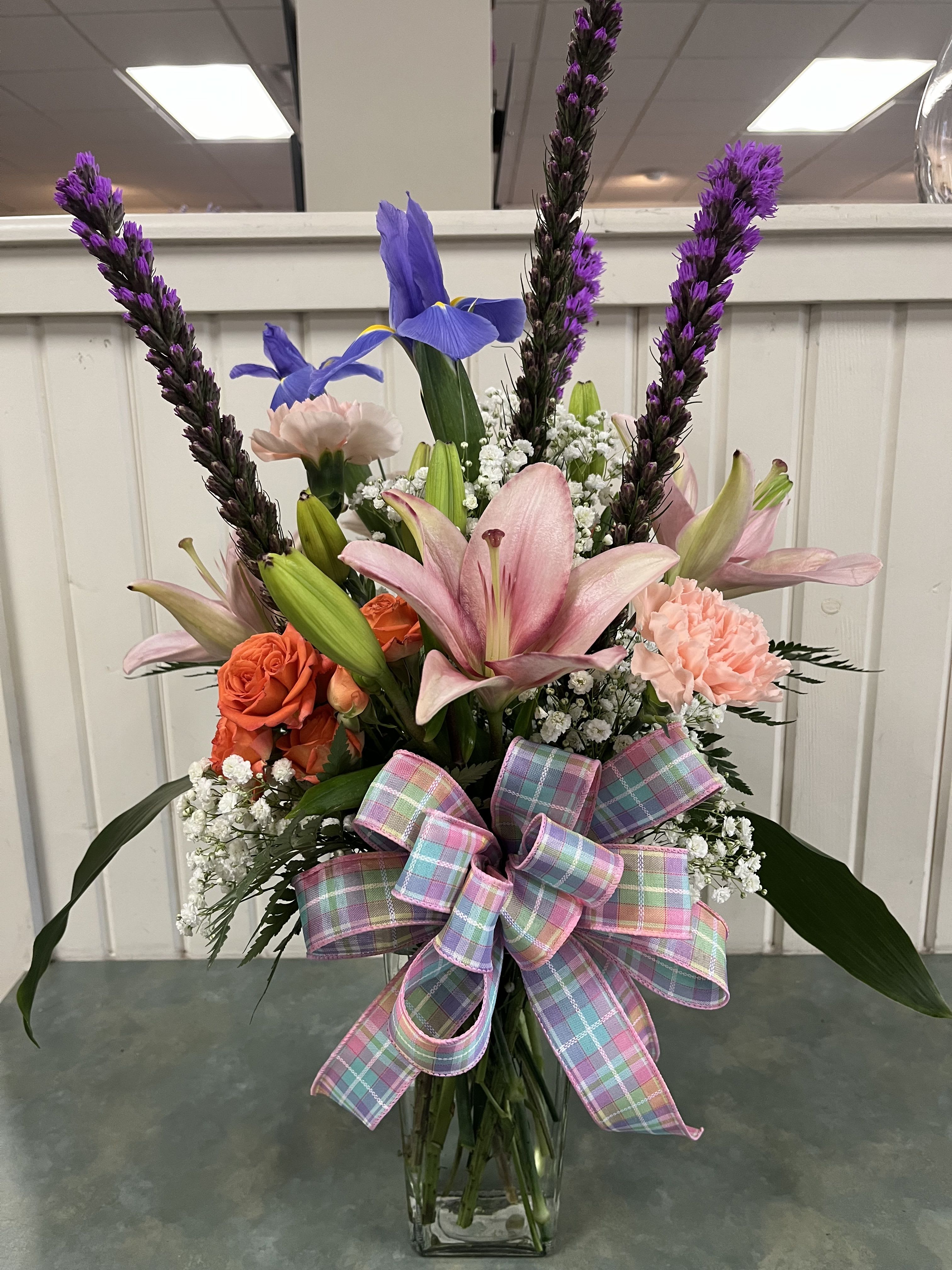 Mixed bouquet with pink lilies, orange roses, and purple spikes in a glass vase