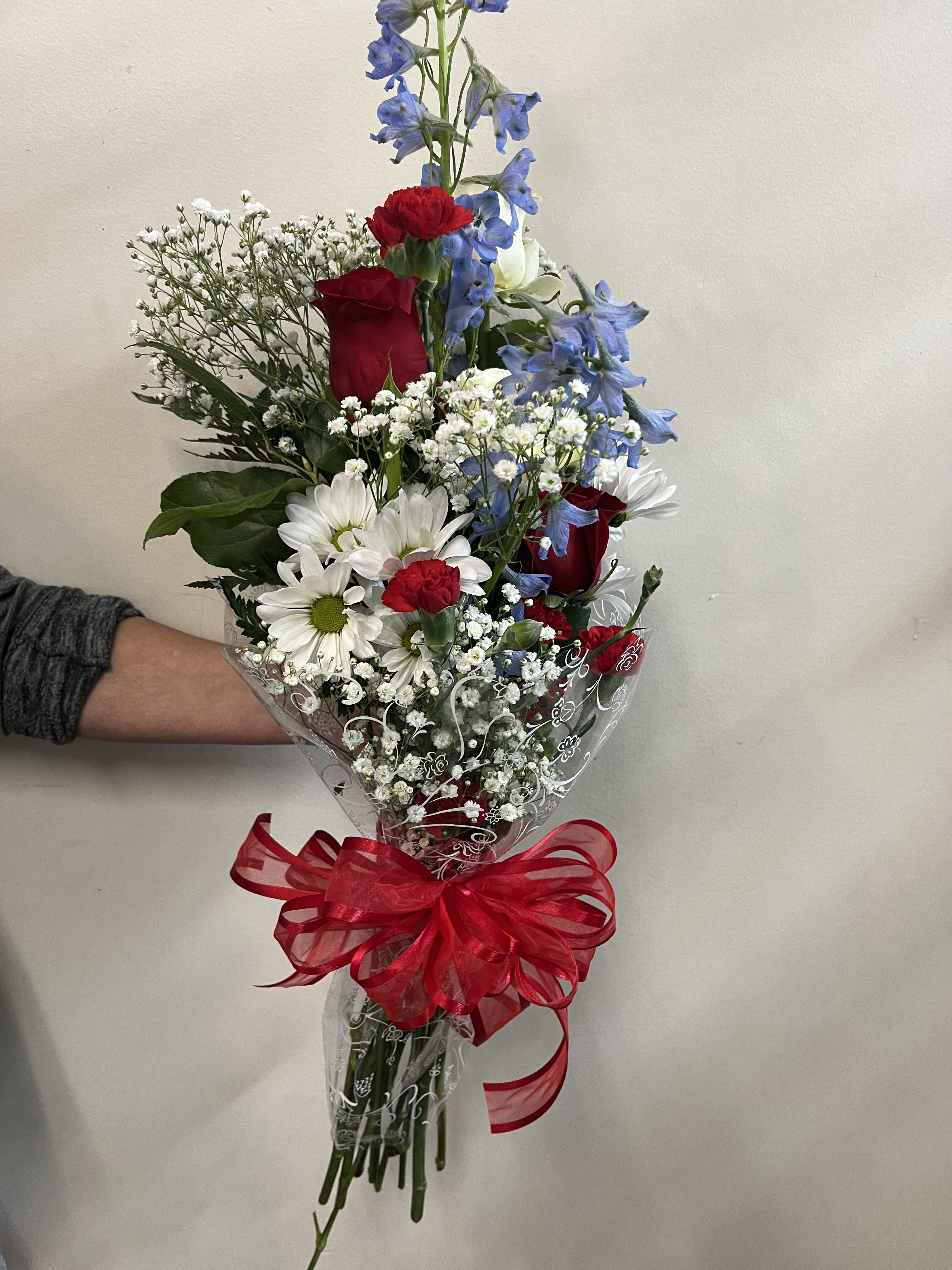 Bouquet of red roses, white daisies, and blue flowers wrapped with a red ribbon