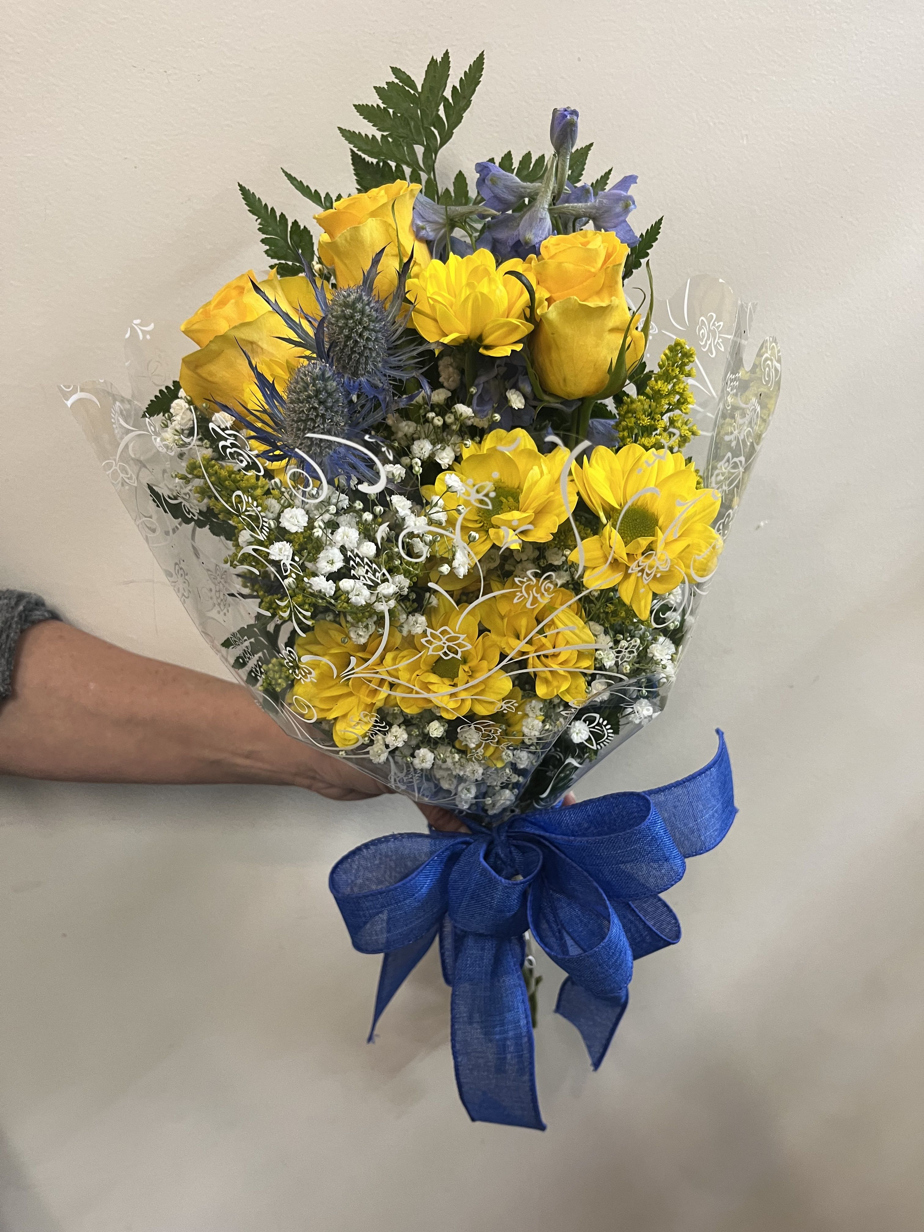 Bouquet of yellow roses and blue thistle wrapped in clear plastic with a blue bow