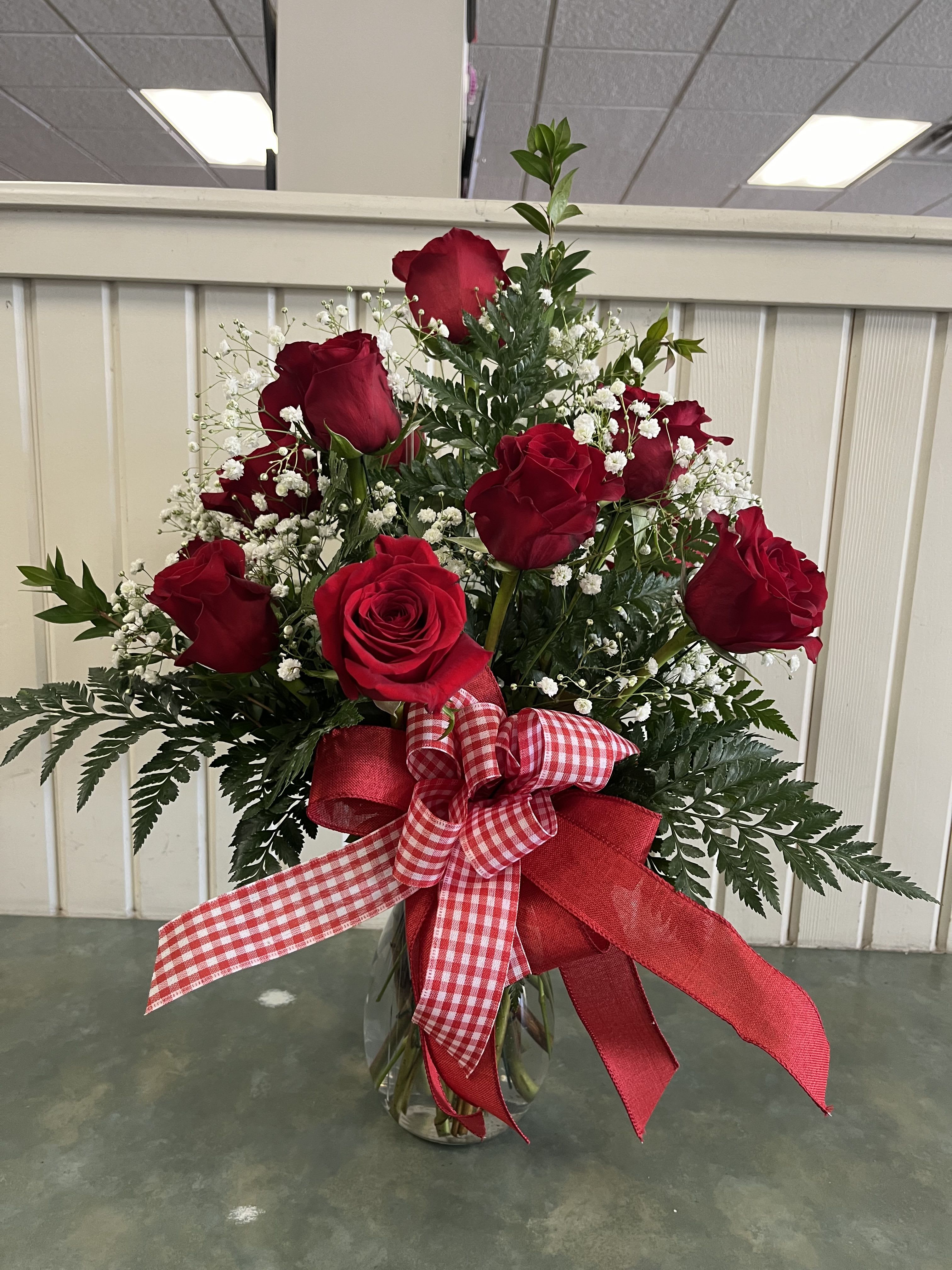 Red roses in a clear glass vase with white baby's breath and a red ribbon bow