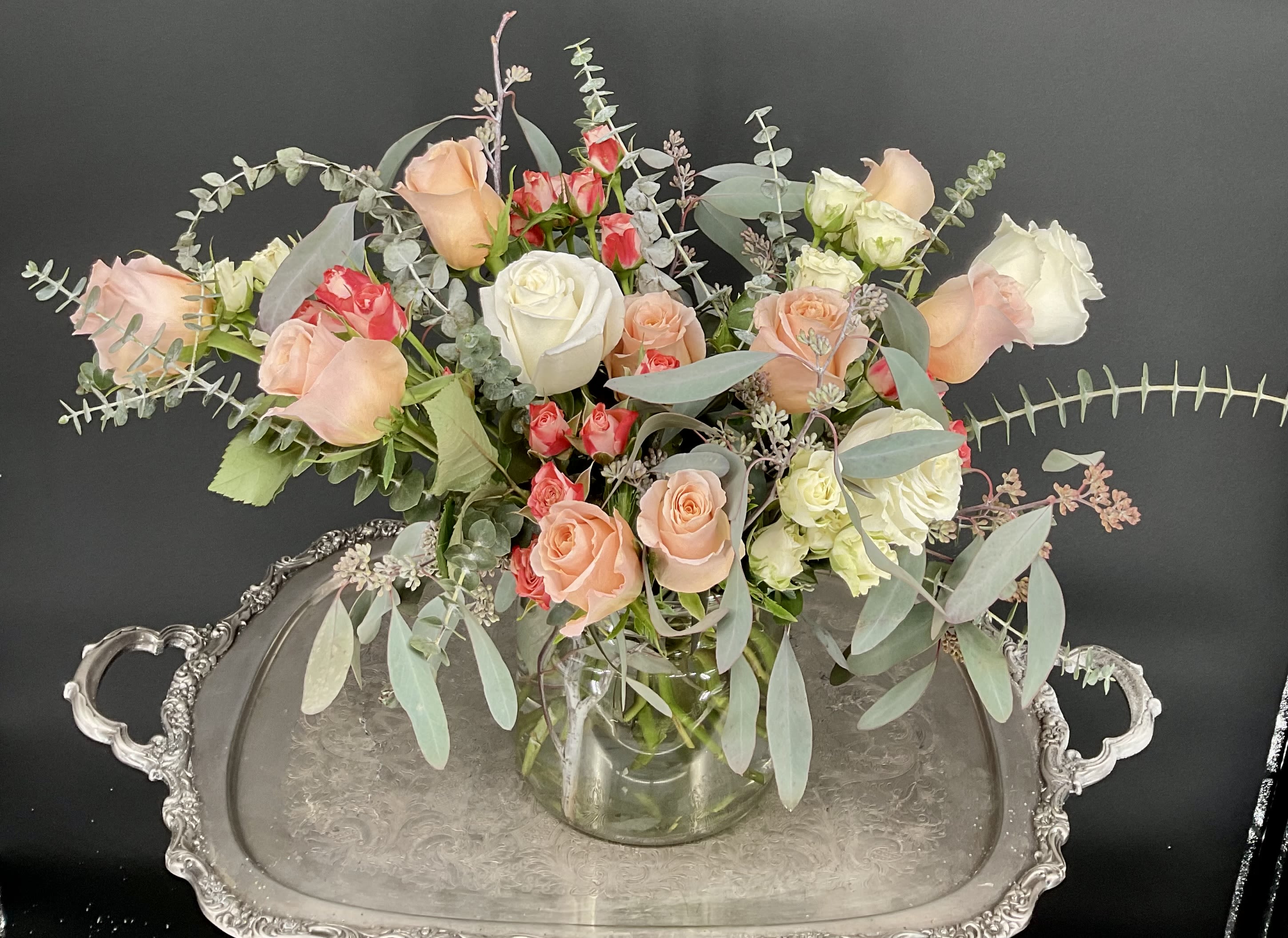 Mixed roses in a clear glass vase with airy eucalyptus on a silver tray