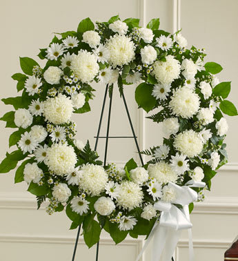 White floral wreath on a black stand with a white ribbon