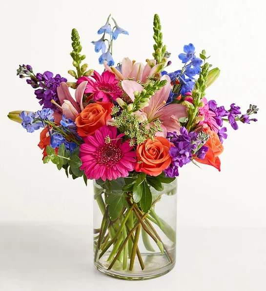Radiant Garden - A fresh-from-the-meadow design makes this colorful bouquet a true delight. Orange roses, blue delphiniums, and more vibrant blooms come together with lush greenery to create a summertime standout certain to lift their spirits.