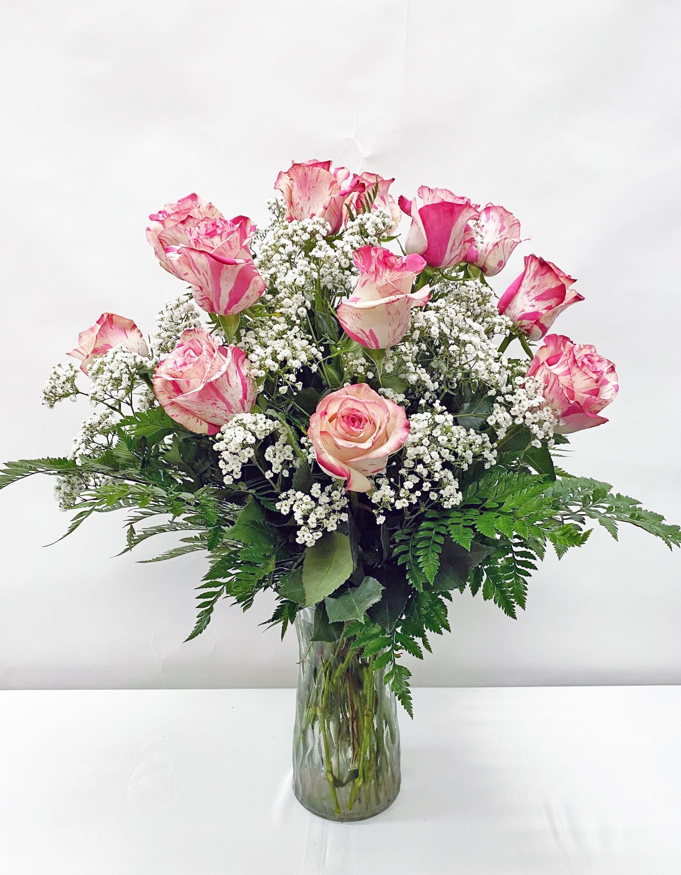 Tall clear vase of pink-tipped white roses with small white filler flowers.