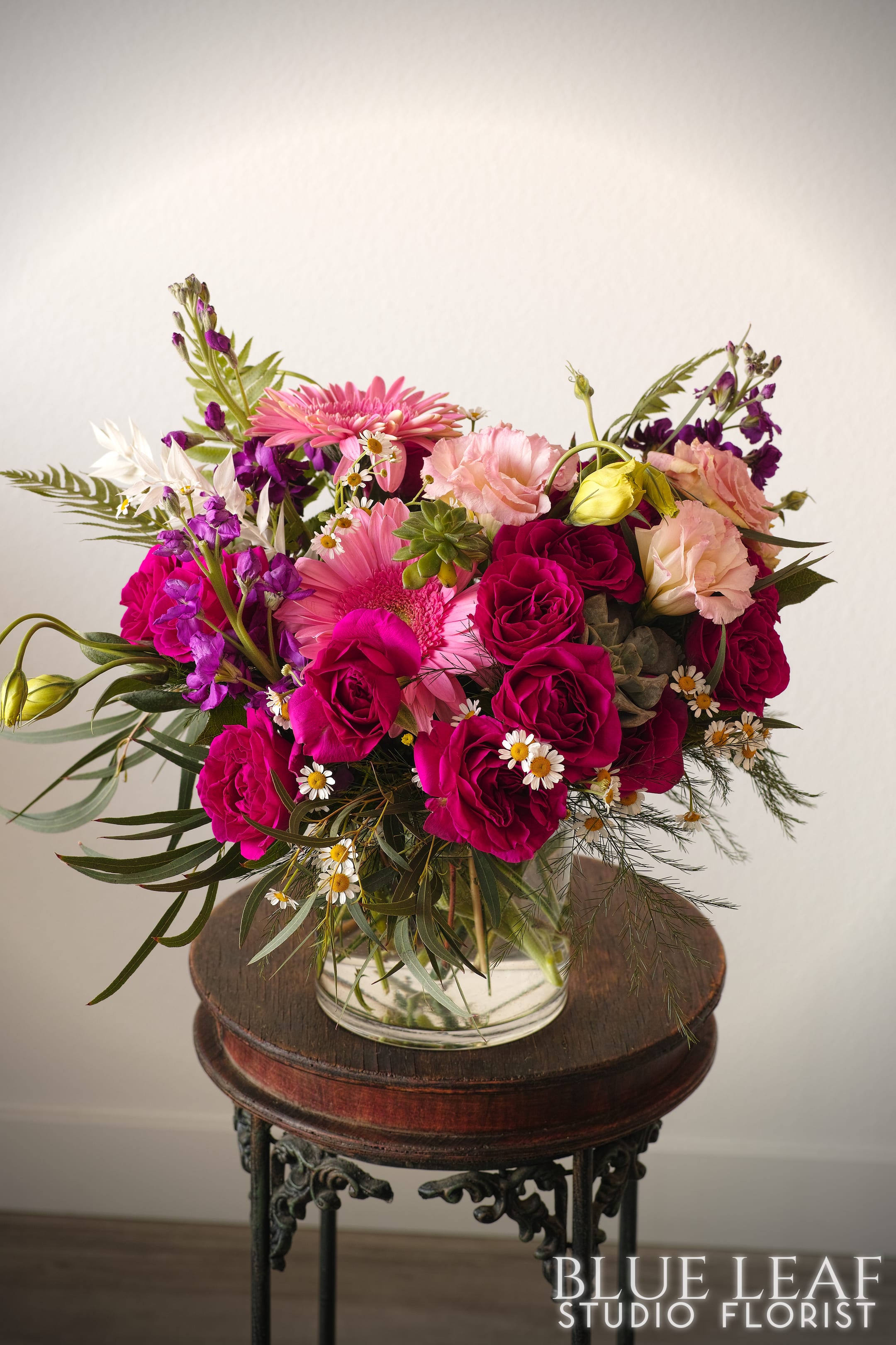 Pink and magenta bouquet with roses, gerbera daisies, and small white daisies in a glass vase
