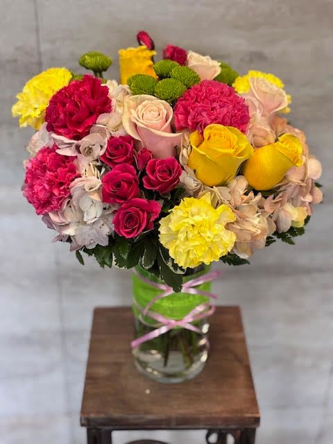 Mixed bouquet of roses, carnations, and hydrangeas in a glass vase