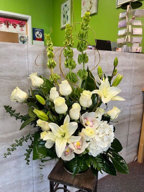 White lilies and roses arranged in a tall vase with green accents