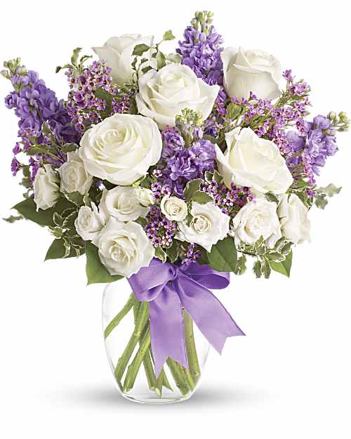 White roses and purple flowers in a clear glass vase with a lavender ribbon