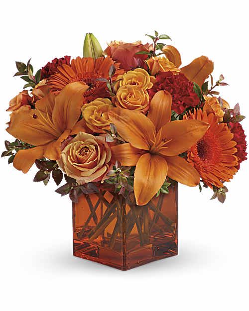 Orange and red flower arrangement in a square glass vase