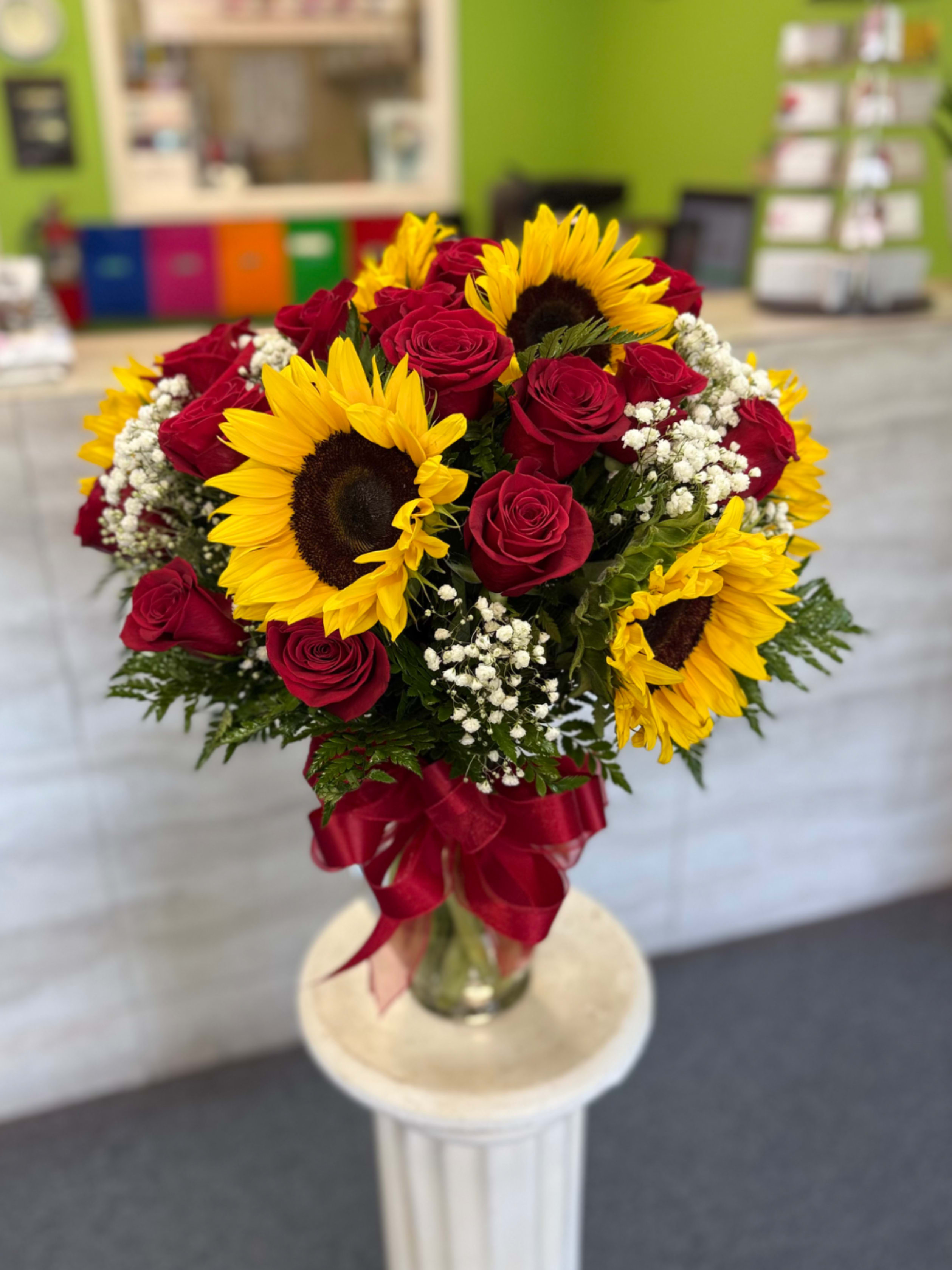 Sun kissed romance  - Bright red roses and sunny yellow sunflowers with white accents in a clear vase tied with red ribbon - bold, cheerful, and romantic, perfect for birthdays, anniversaries, or celebratory gifting. 