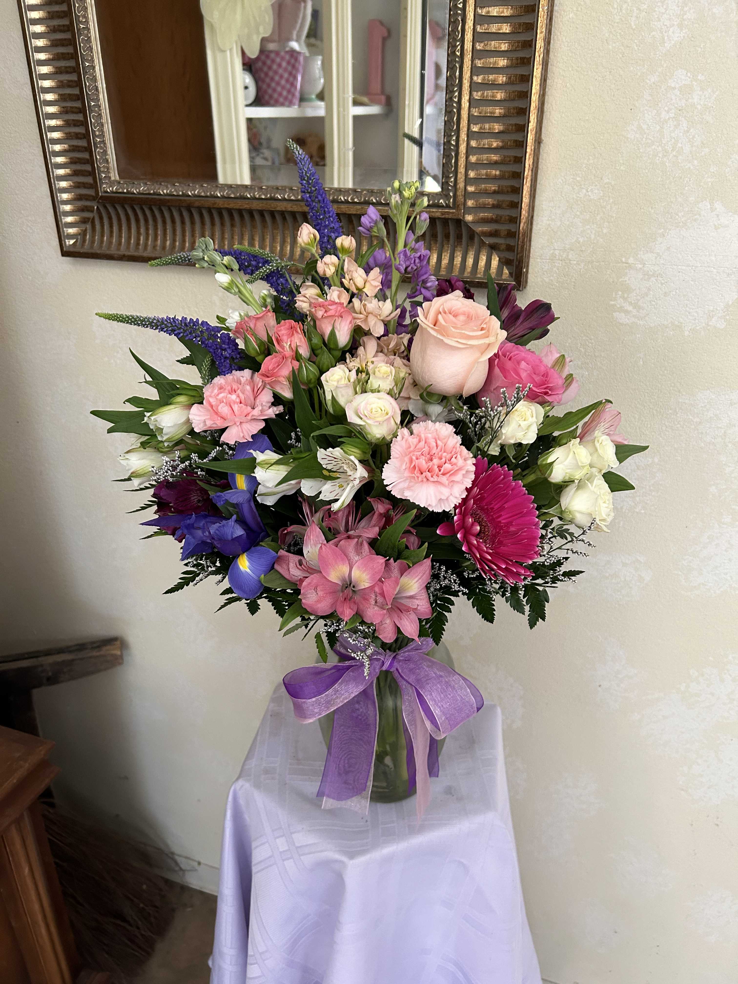 Mixed bouquet of pink, purple, and white flowers in a glass vase with a purple ribbon