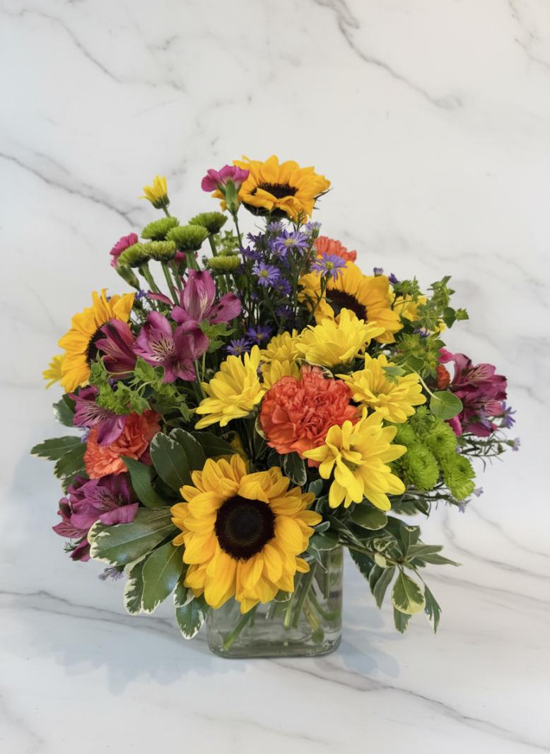Bright mixed bouquet with sunflowers, daisies, and alstroemeria in a glass vase