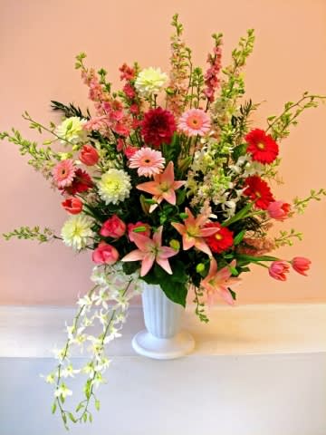 Tall mixed flower arrangement in a white vase with pink, red, and white blooms