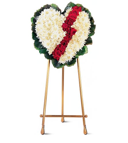 Heart-shaped funeral wreath of white flowers with a red rose stripe on an easel