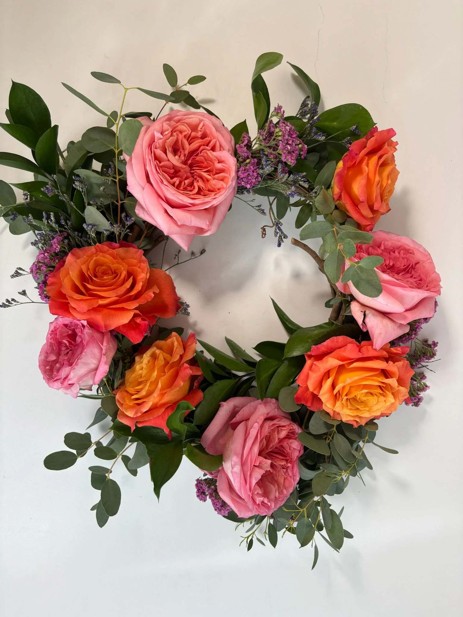 Circular wreath of pink and orange roses with purple filler flowers