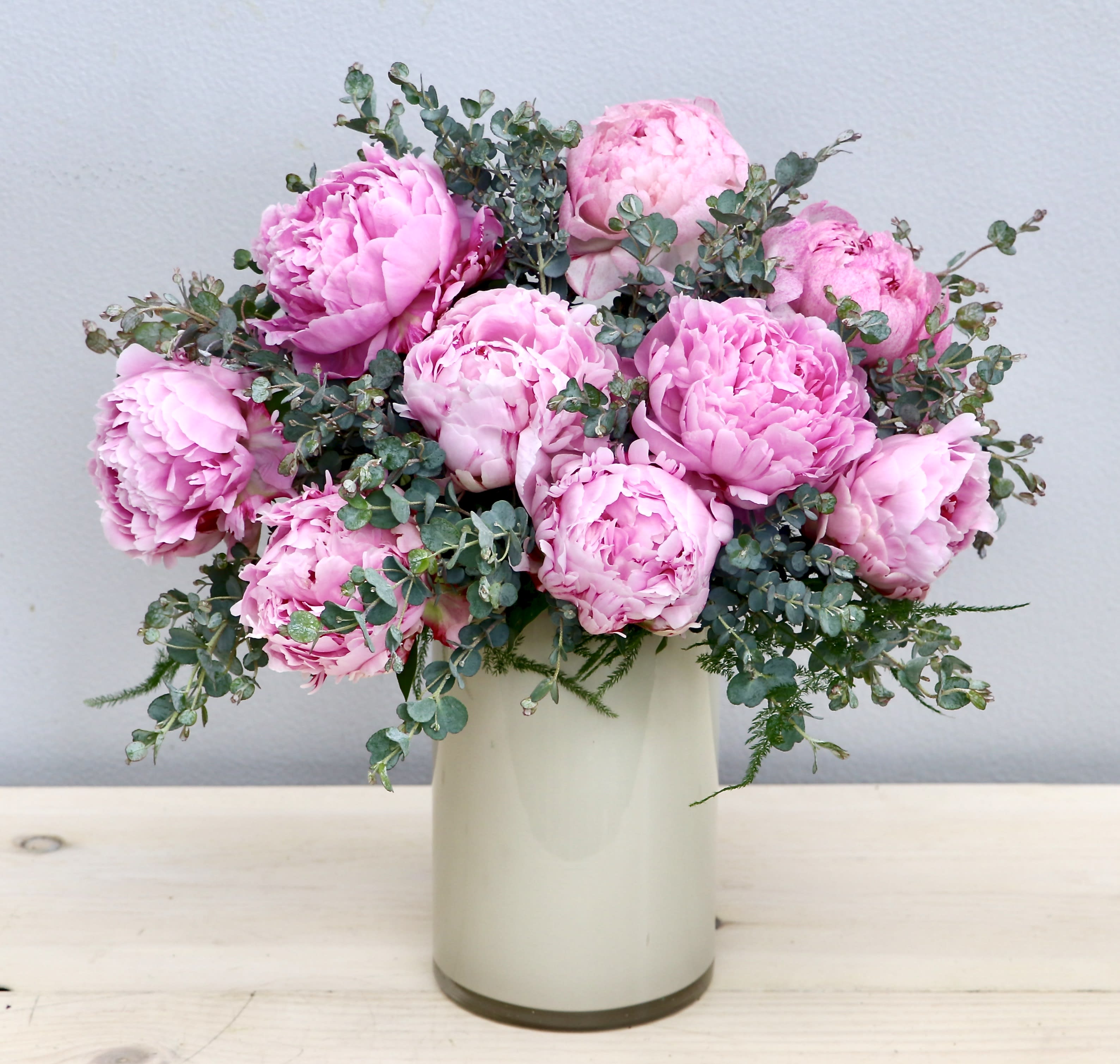 Arrangement of pink peonies in a tall cream-colored vase