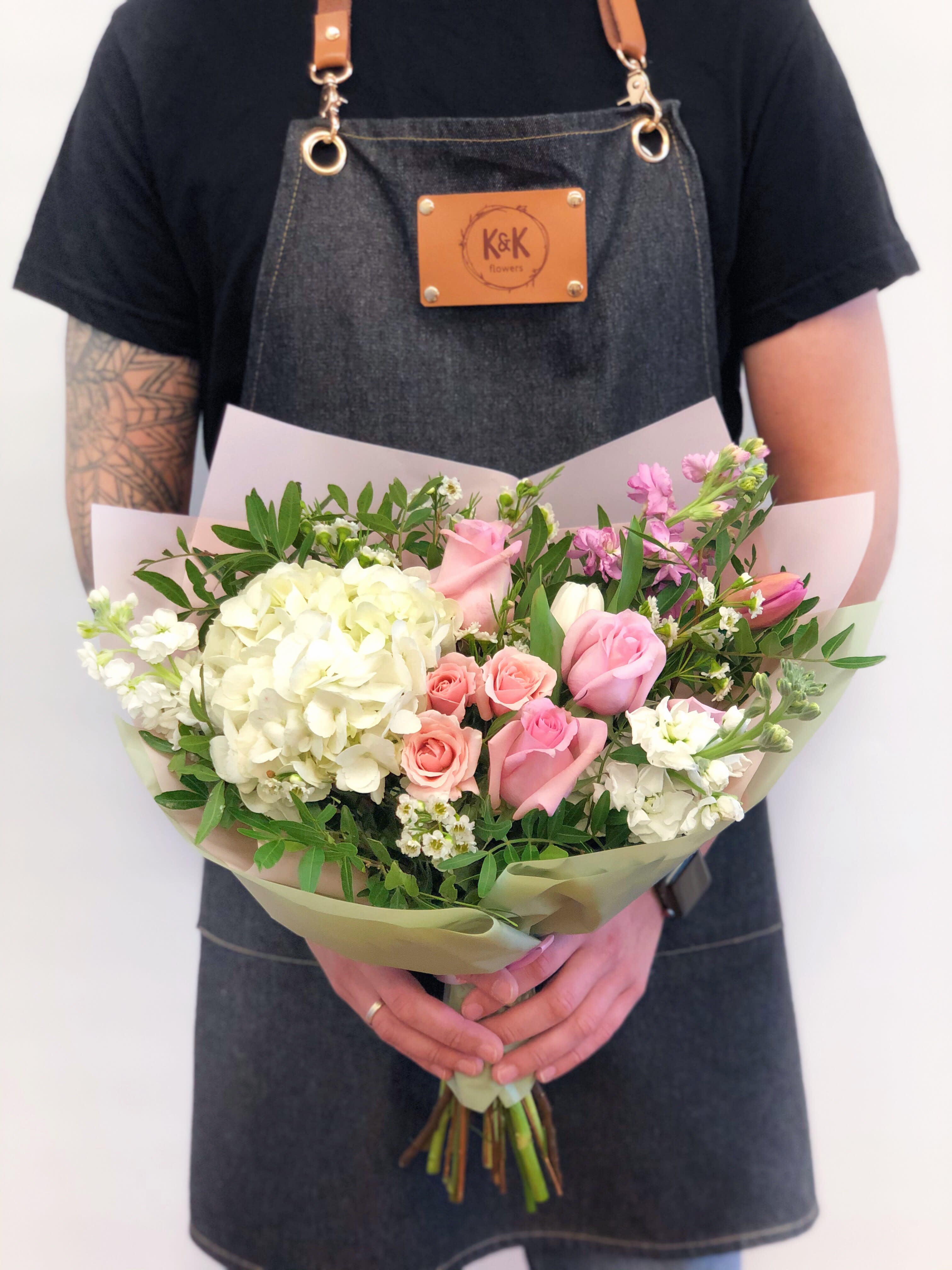Handheld bouquet of pink and white flowers wrapped in pale paper