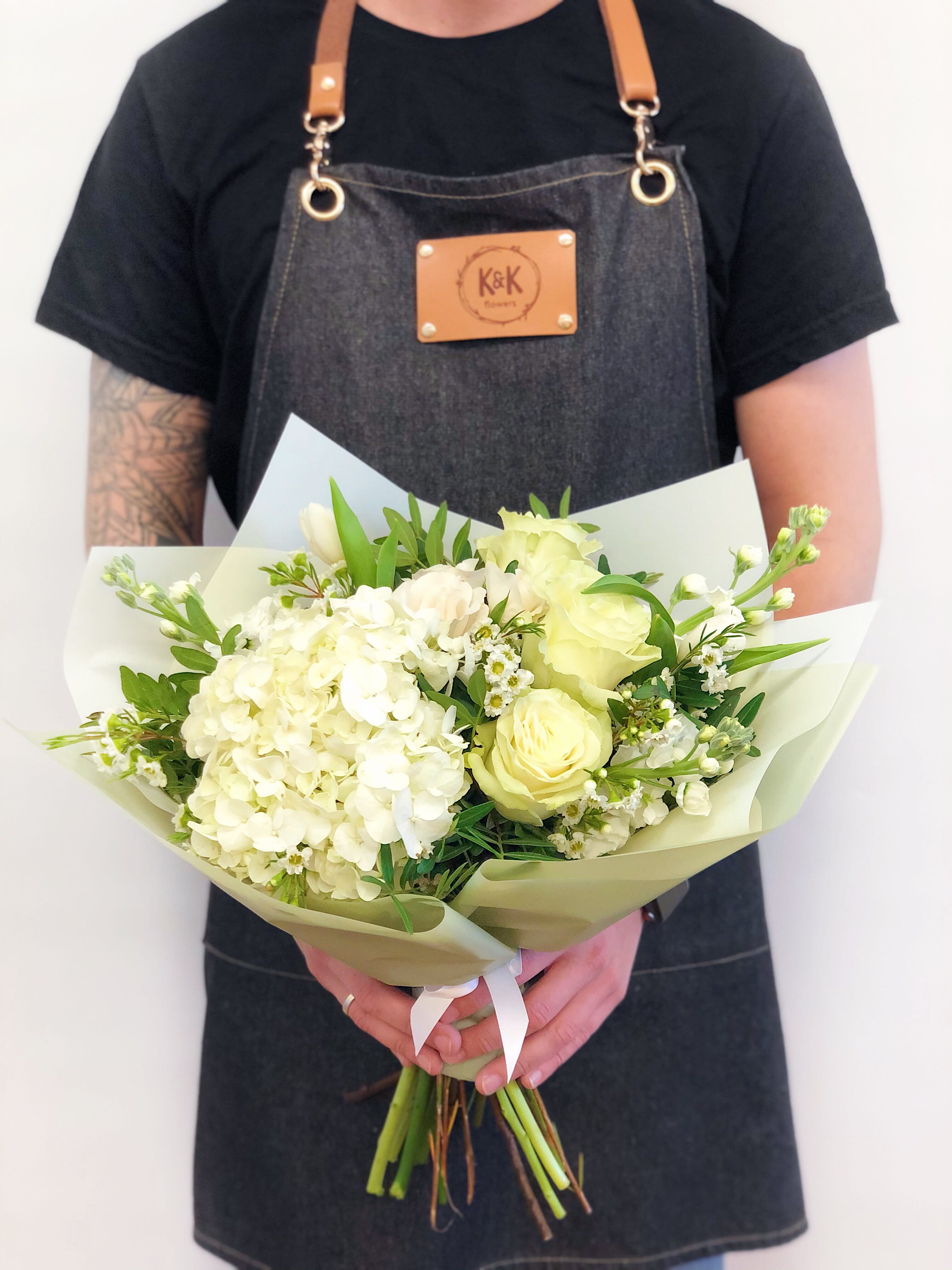 Handheld bouquet of white and pale yellow flowers wrapped in paper
