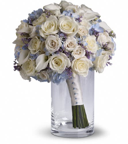 White rose bouquet with blue accents in a clear glass vase