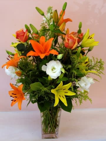 Bouquet of orange and yellow lilies with white blooms in a clear glass vase