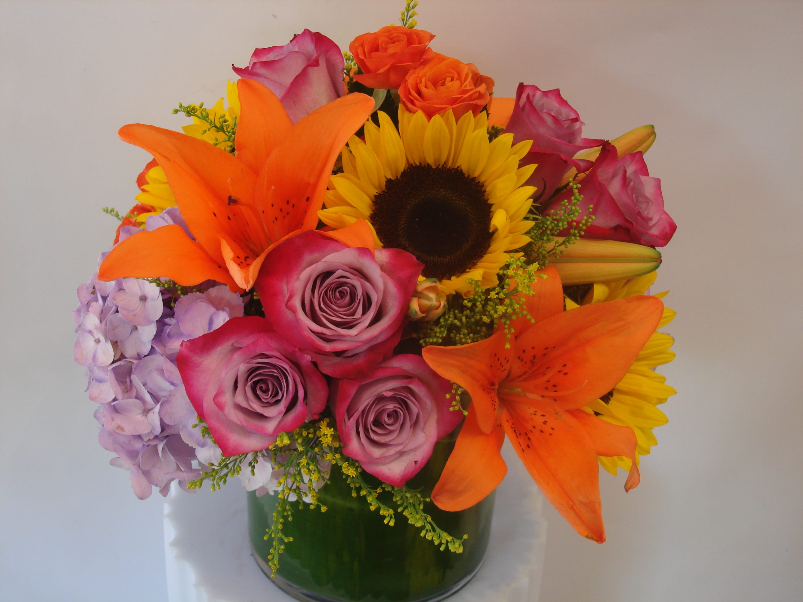 Mixed bouquet with roses, lilies, sunflower, and hydrangea in a glass vase