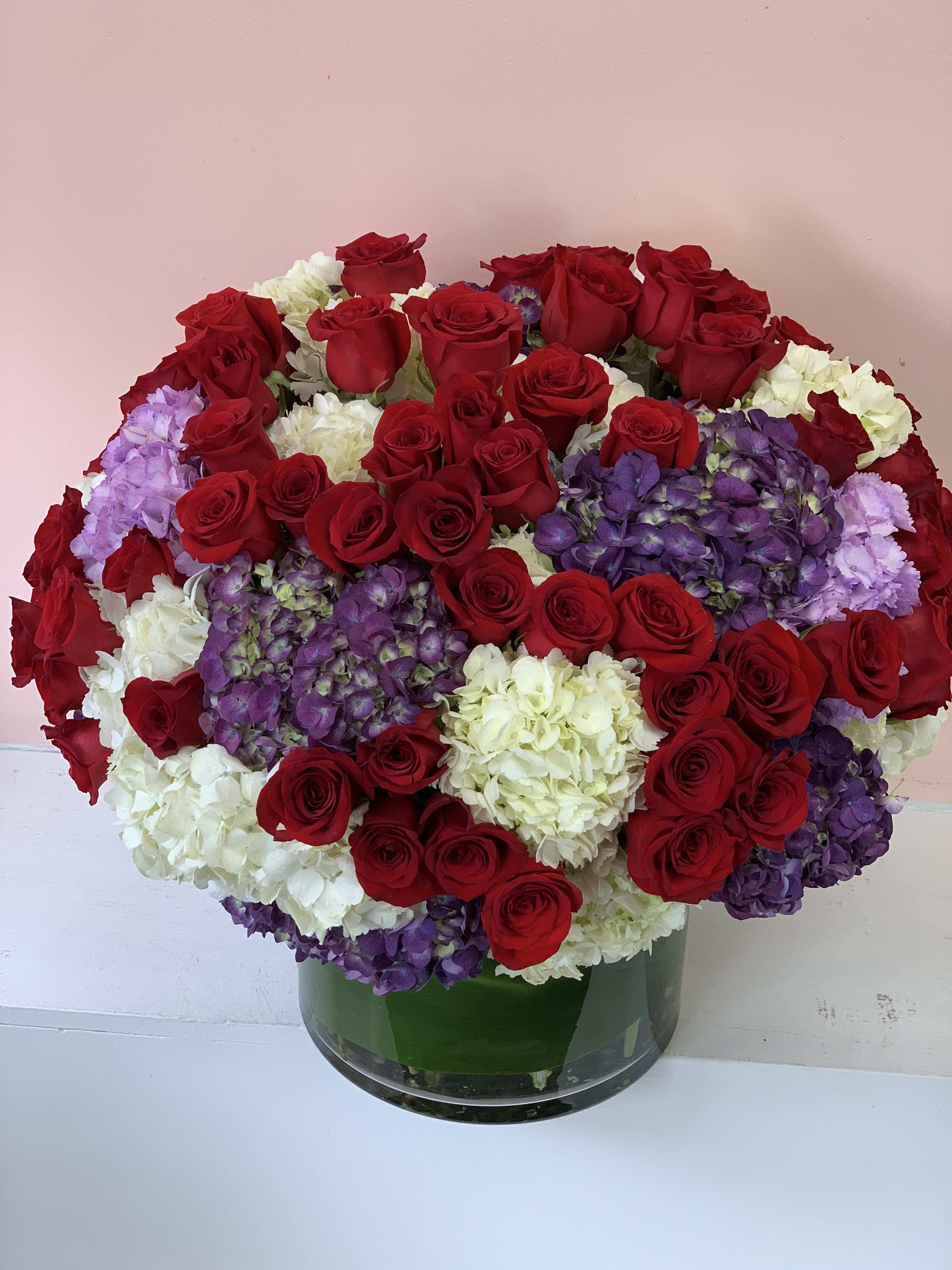 Large bouquet of red roses, white hydrangeas, and purple hydrangeas in a glass vase