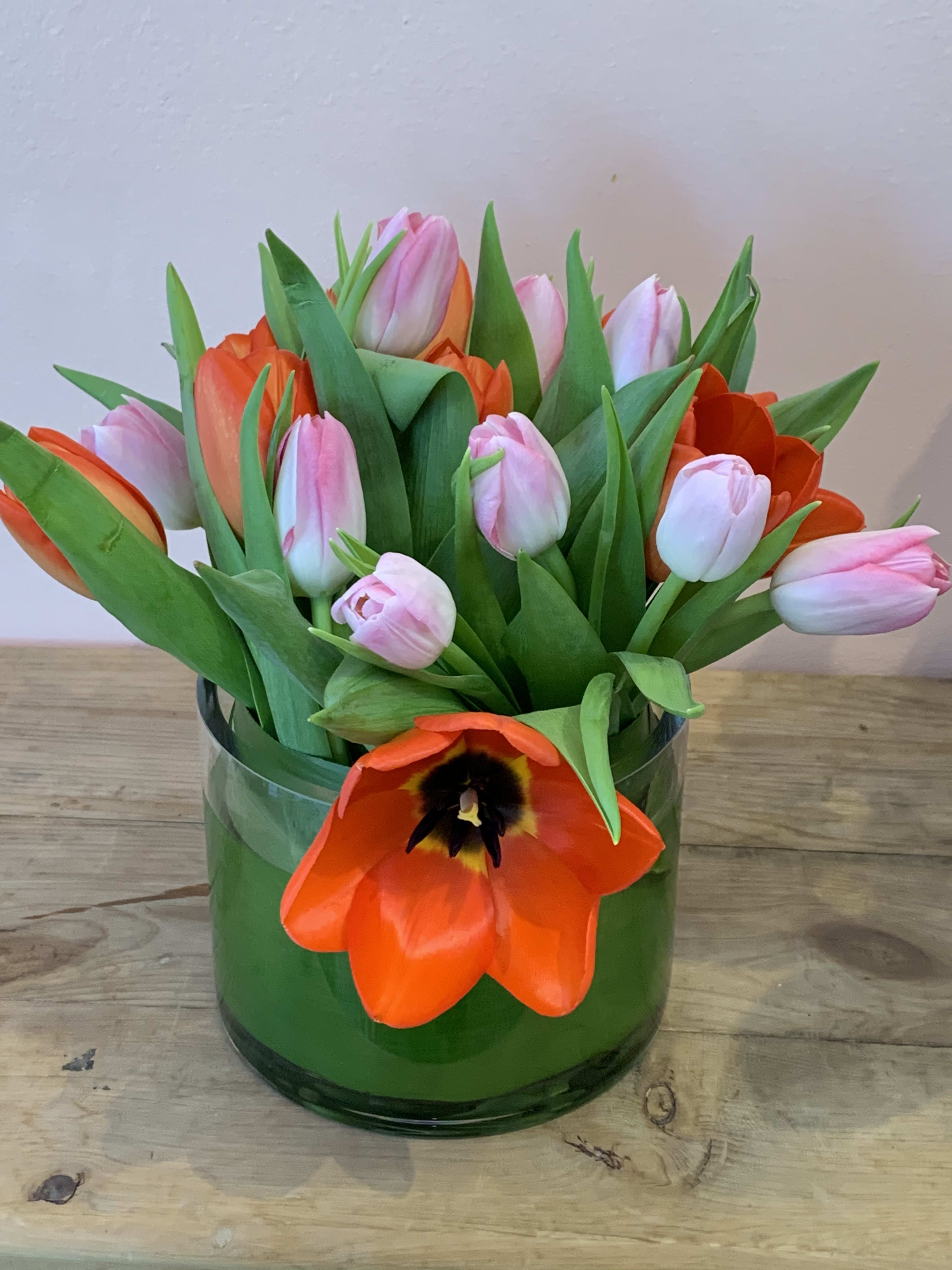 Pink and orange tulips arranged in a green glass vase