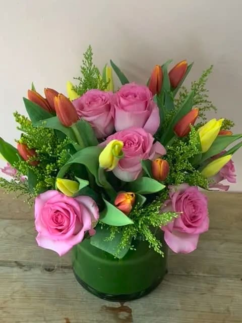 Pink roses and orange-yellow tulips in a green glass vase