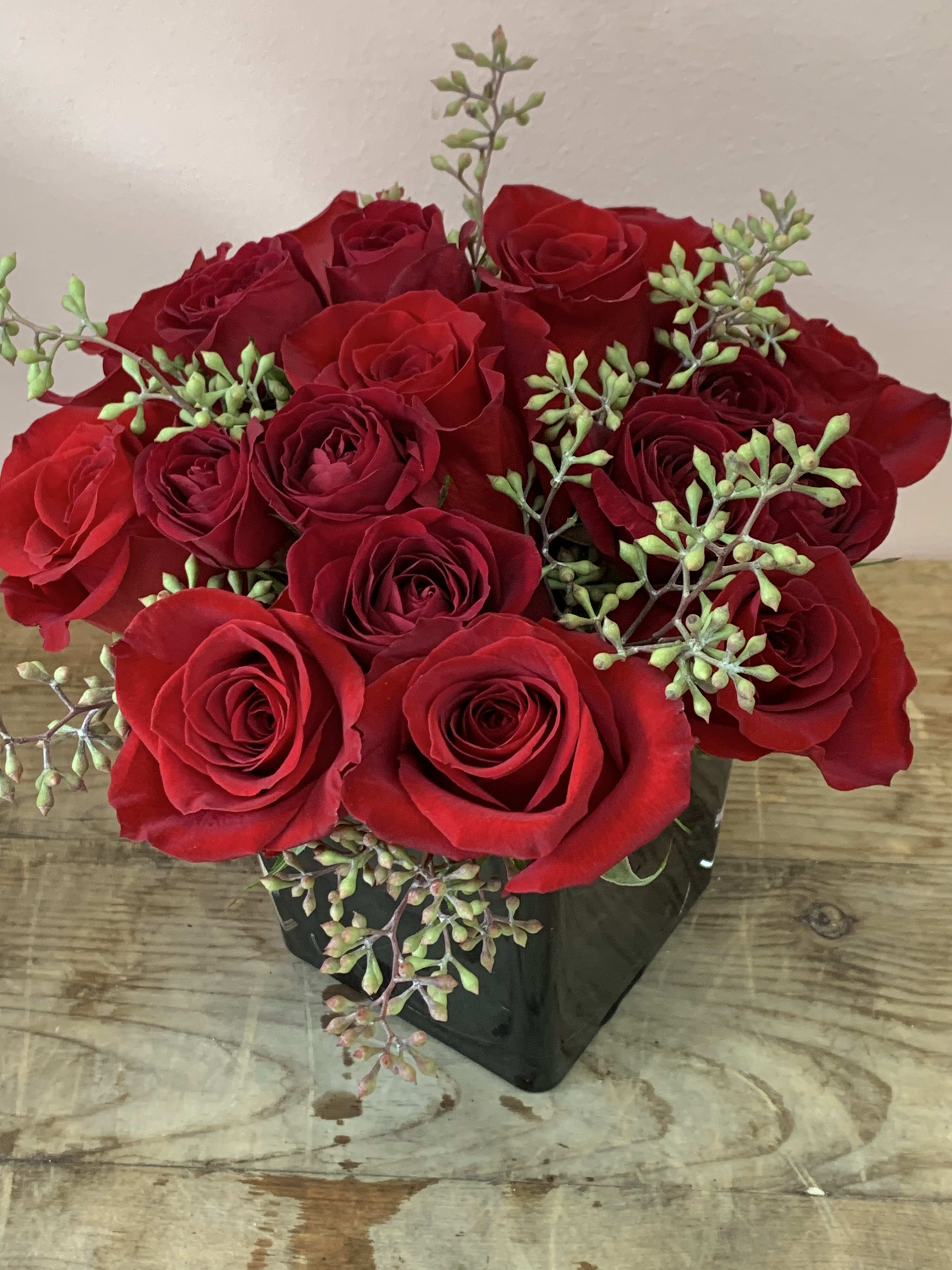 Red roses arranged in a black square vase with green filler sprigs