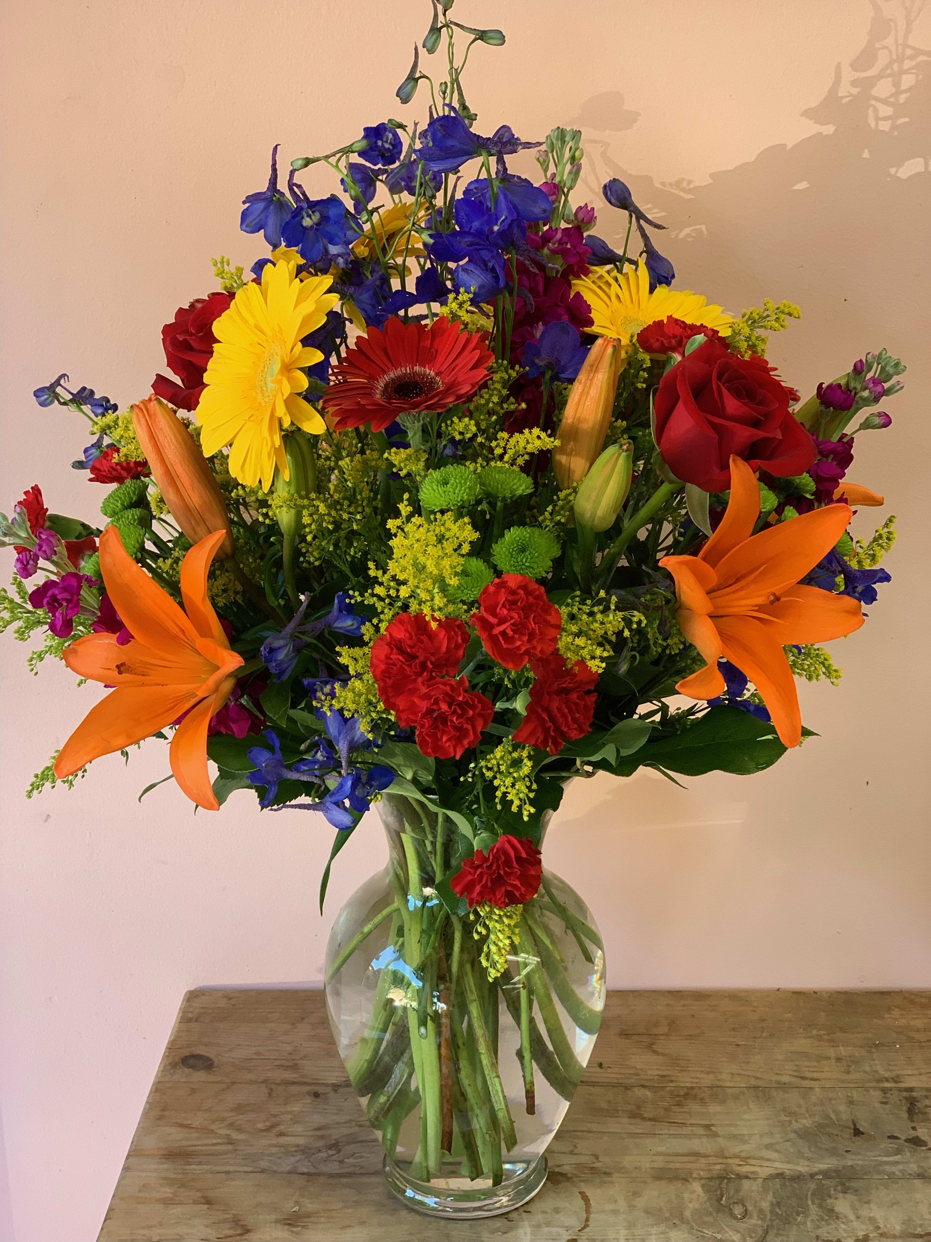 Colorful mixed bouquet in a clear glass vase with lilies, roses, and daisies