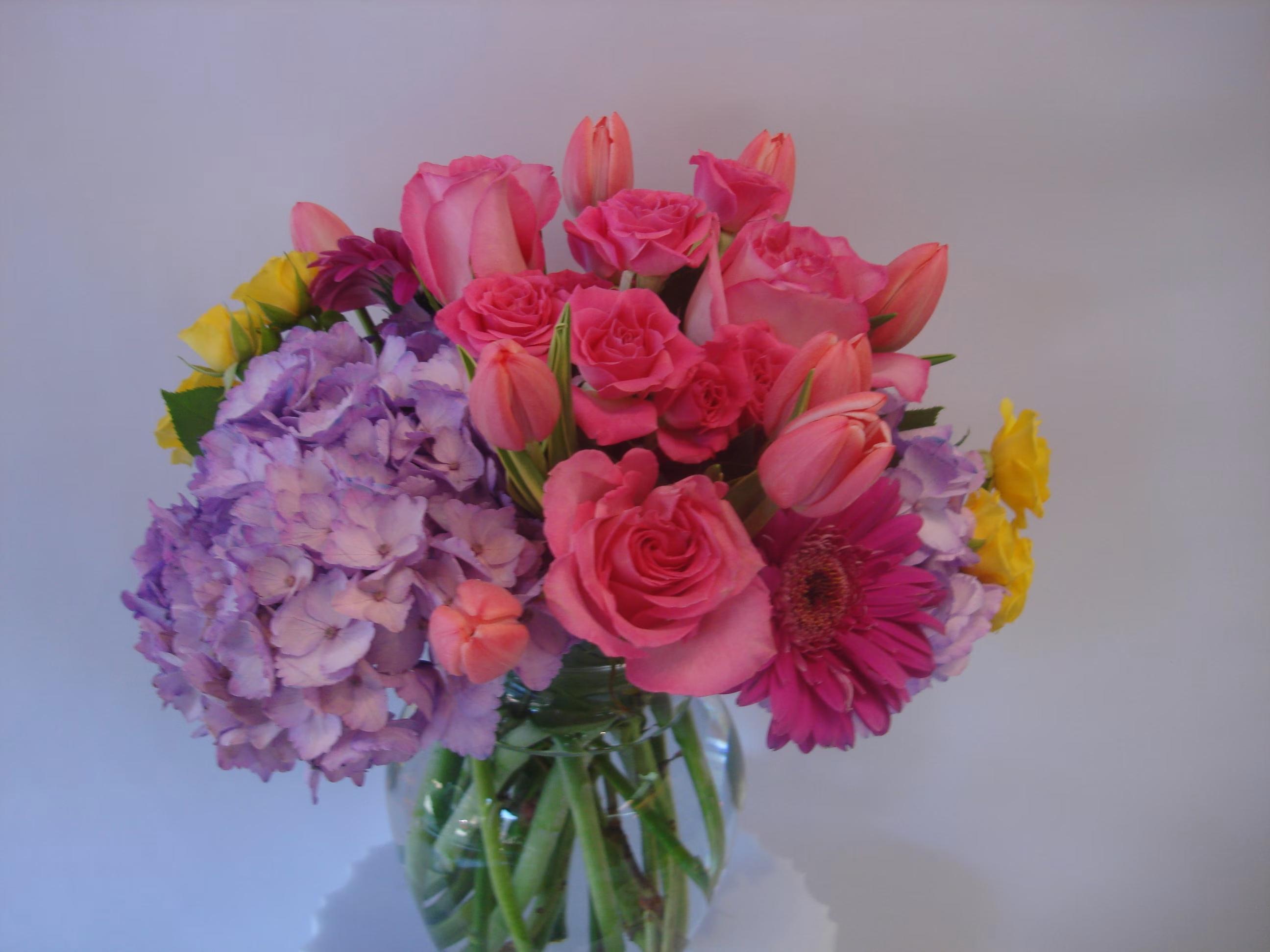Mixed bouquet of pink roses, tulips, hydrangeas, and a gerbera daisy in a glass vase