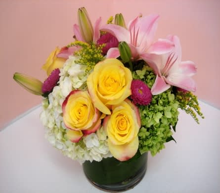 Bouquet of yellow roses, pink lilies, and white hydrangeas in a glass vase