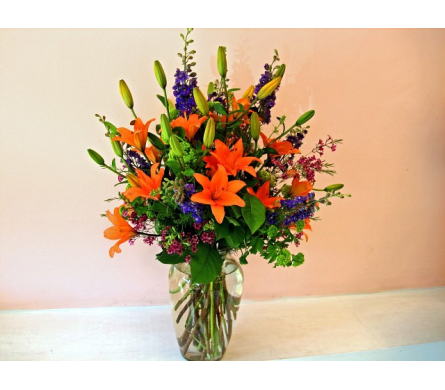 Orange lilies and purple flowers in a clear glass vase