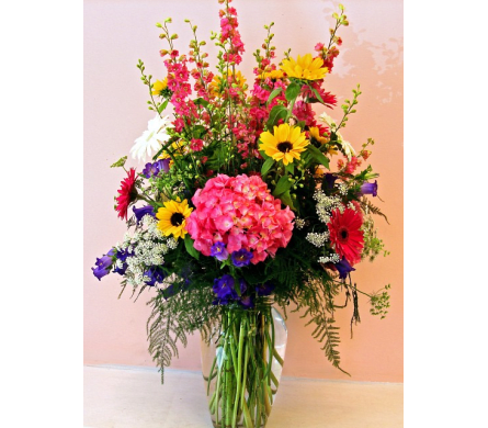 Tall mixed bouquet in a clear glass vase with pink, yellow, red, white, and purple flowers