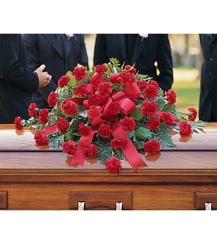 Red carnation casket spray with ribbon on a wooden coffin