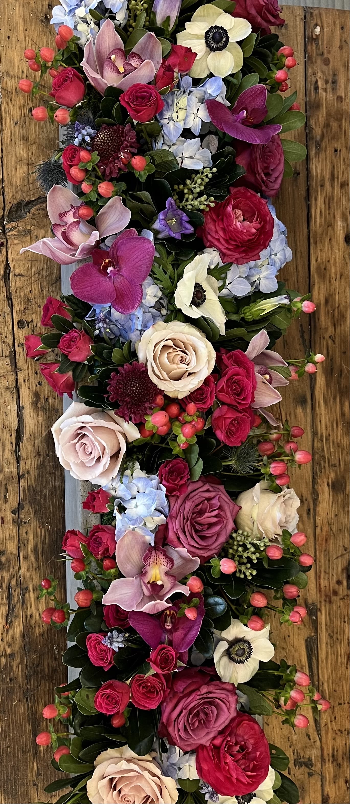 Vertical floral arrangement with roses, orchids, and pale anemones