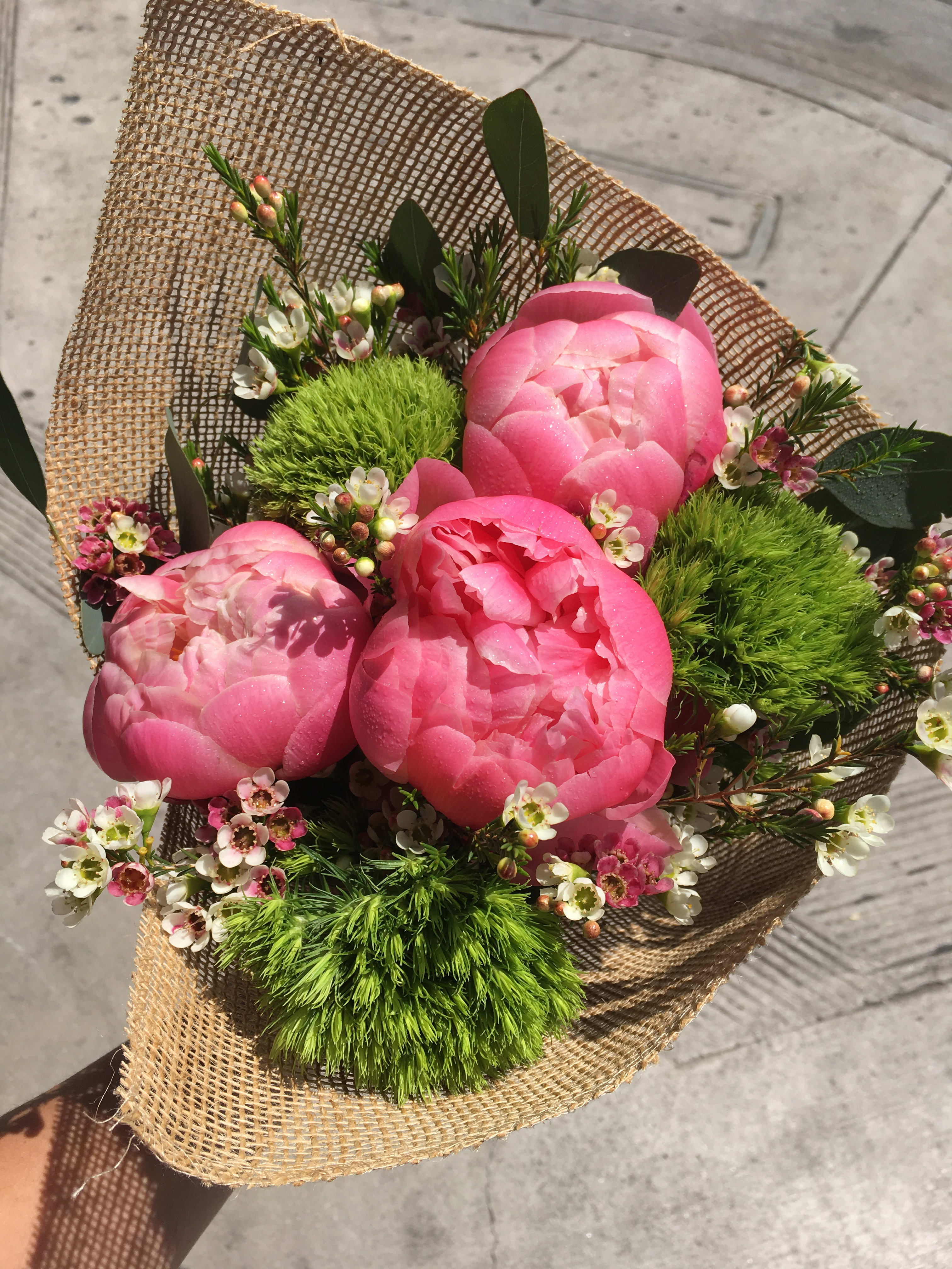 Pink peony bouquet with small white blossoms wrapped in burlap