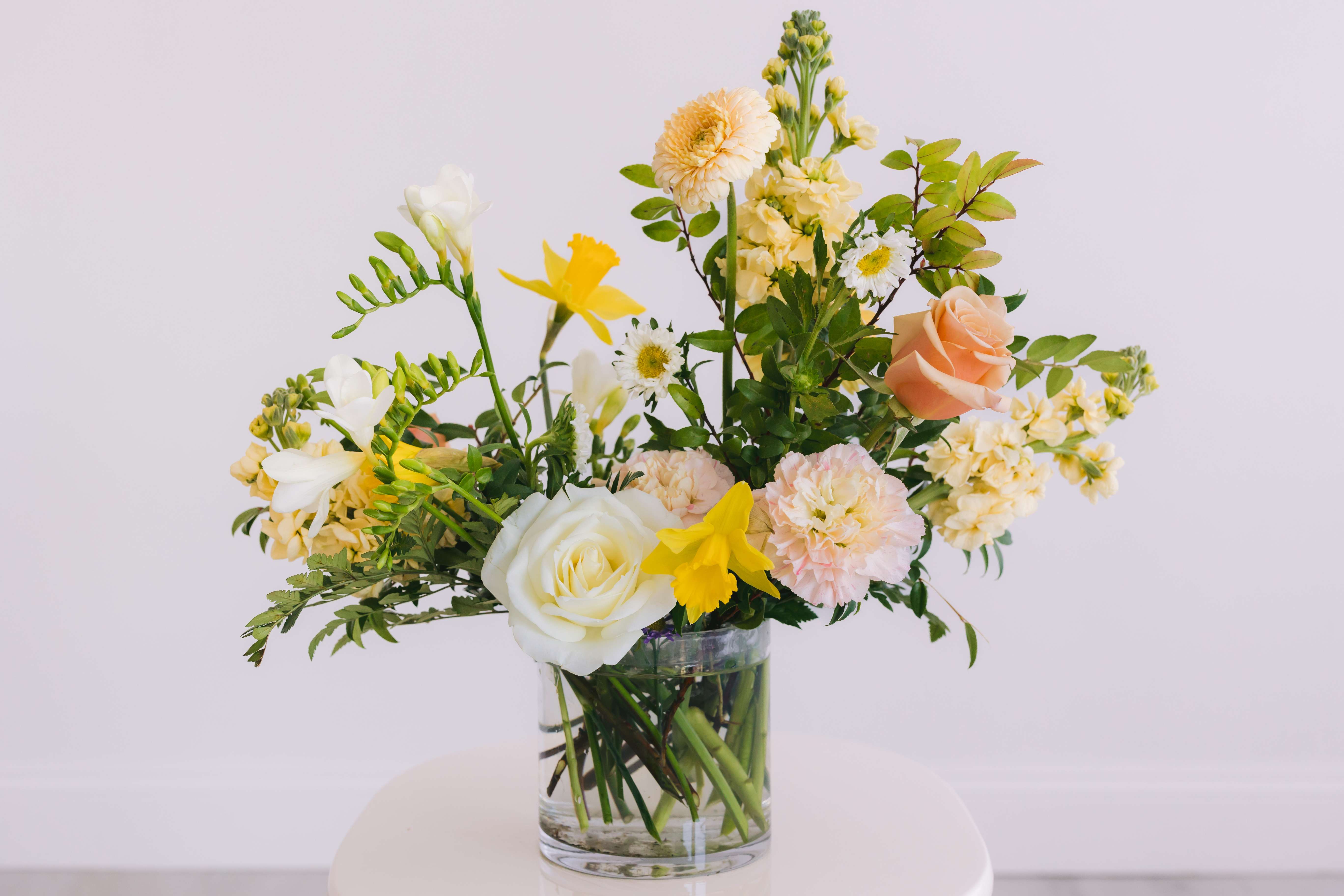 THE SIGNATURE - Designed in our signature style: a lush garden-style mix of seasonal blooms and foliage.  Each arrangement comes in a glass cylinder vase; working with each stem’s natural curves allowing for each one to be unique.  Our team of expert designers will carefully select a seasonal floral and color palette for a custom and beautifully designed arrangement.  Each bouquet is packaged with white tissue and wrapped in our black logo textured ribbon.  *Please note that our color and floral palette changes from week to week.  All substitutions will be of equal value. 