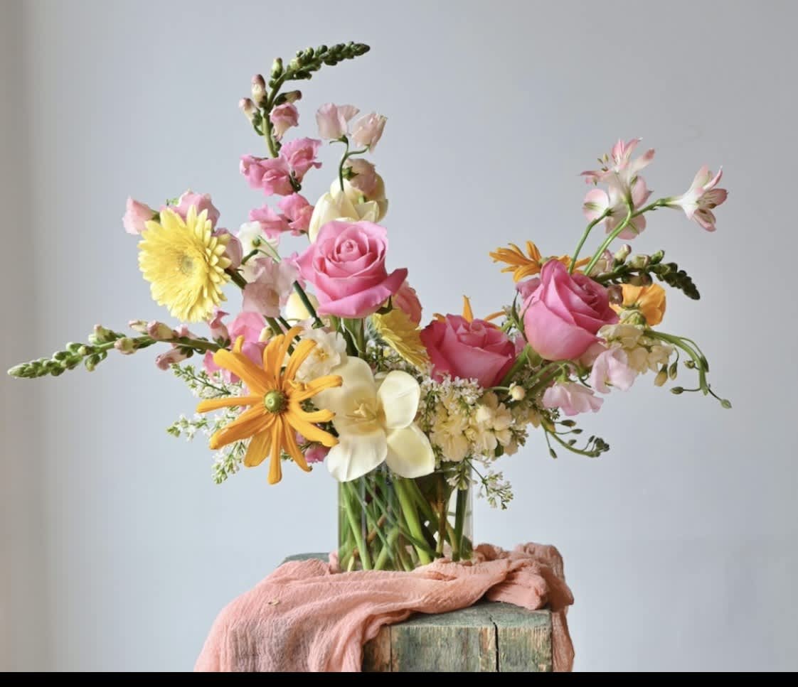 Mixed bouquet of pink roses, yellow daisies, and white flowers in a glass vase