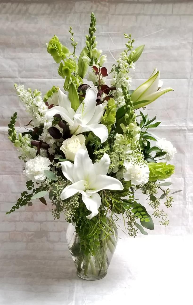 White lilies and green blooms in a clear glass vase