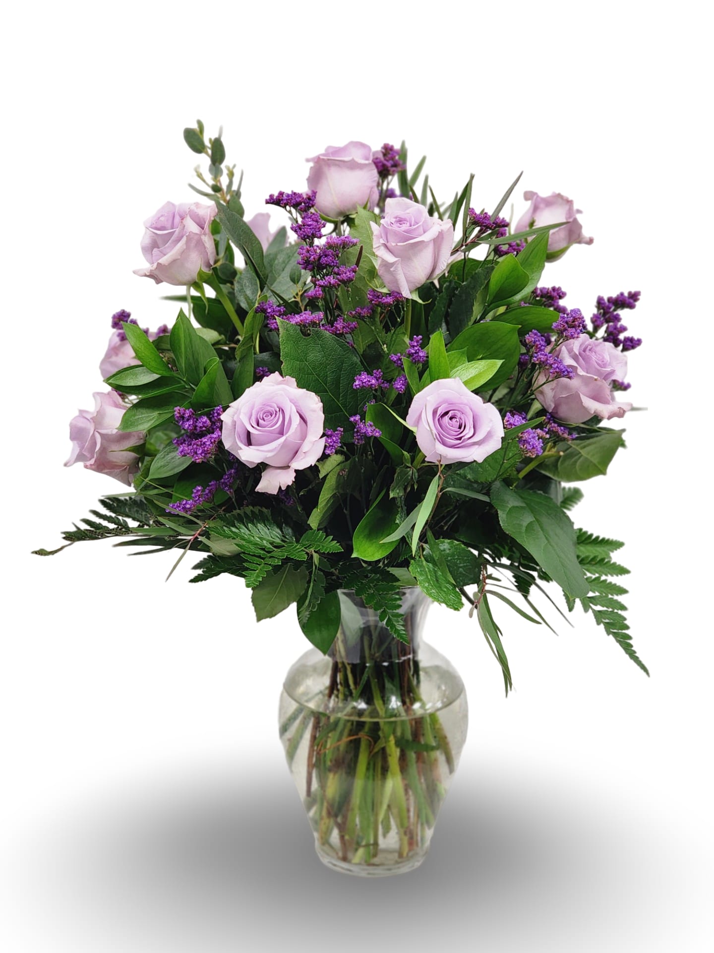 Lavender roses and small purple flowers arranged with lush foliage in a clear glass vase