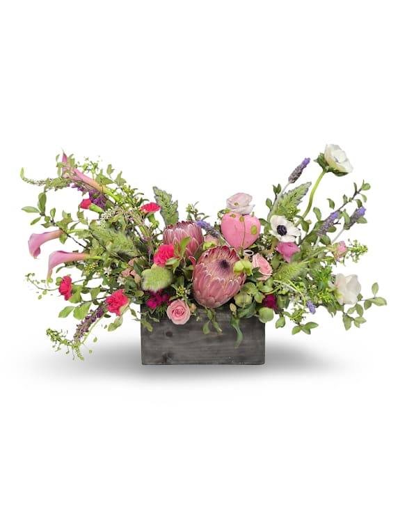 Garden Glamour  - Garden Glamour is a bold and elegant arrangement inspired by a lush garden in full bloom. Featuring a striking mix of pink tones, textured blooms, and flowing greenery, this design feels both natural and refined. Styled in a modern container, it makes a stunning statement for any special occasion. Approximately 11x22 inches.