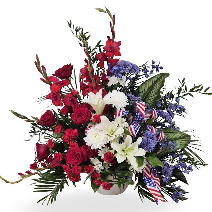Freedom's Tribute Podium Arrangement - Freedom's Tribute is a striking red, white, and blue podium arrangement designed to honor and remember with dignity and pride. featuring a bold mix of seasonal blooms accented with patriotic ribbon and lush greenery, this full arrangement makes a meaningful statement for services and ceremonies. Approx. 36" x 36"
