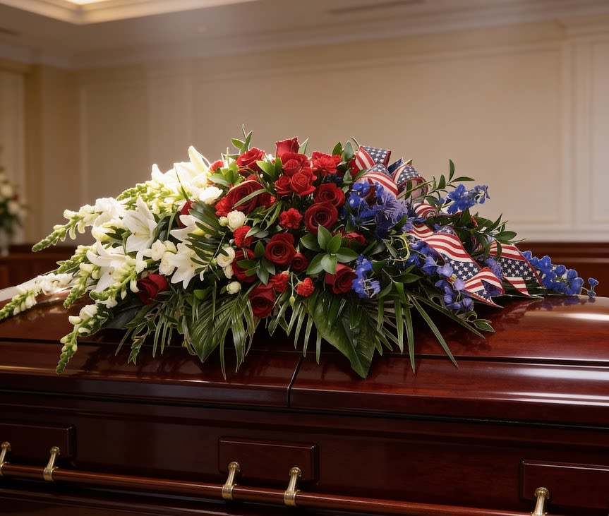 Freedom's Tribute Casket Spray - Freedom's Tribute Casket Spray is a classic red, white and blue arrangement designed to honor a life with pride and respect. Featuring roses, seasonal blooms, lush greenery, and patriotic ribbon, this large half-casket spray creates a meaningful and dignified tribute.  Standard version approx. 12" H x 55" L x 22" W  This standard version is designed as a large half-casket piece. The premium version extends into a full-length spray to cover the casket for a fuller presentation.