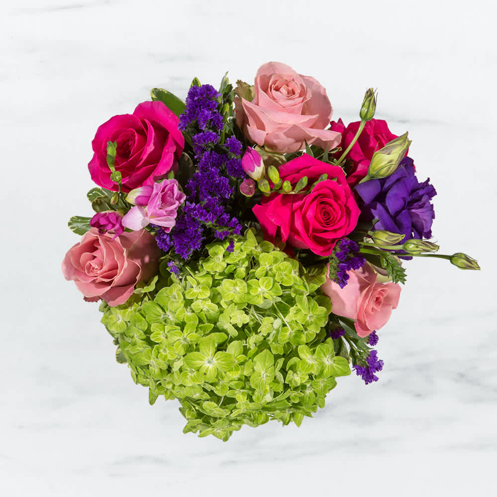 Spring Fling by BloomNation™ - This arrangement includes hot pink roses, pink roses, green hydrangea, freesia, lisianthus, purple statice. Spring Fling by BloomNation™ is a great gift for a birthday, get well, or just because.   APPROXIMATE DIMENSIONS: 12" H X 12" W