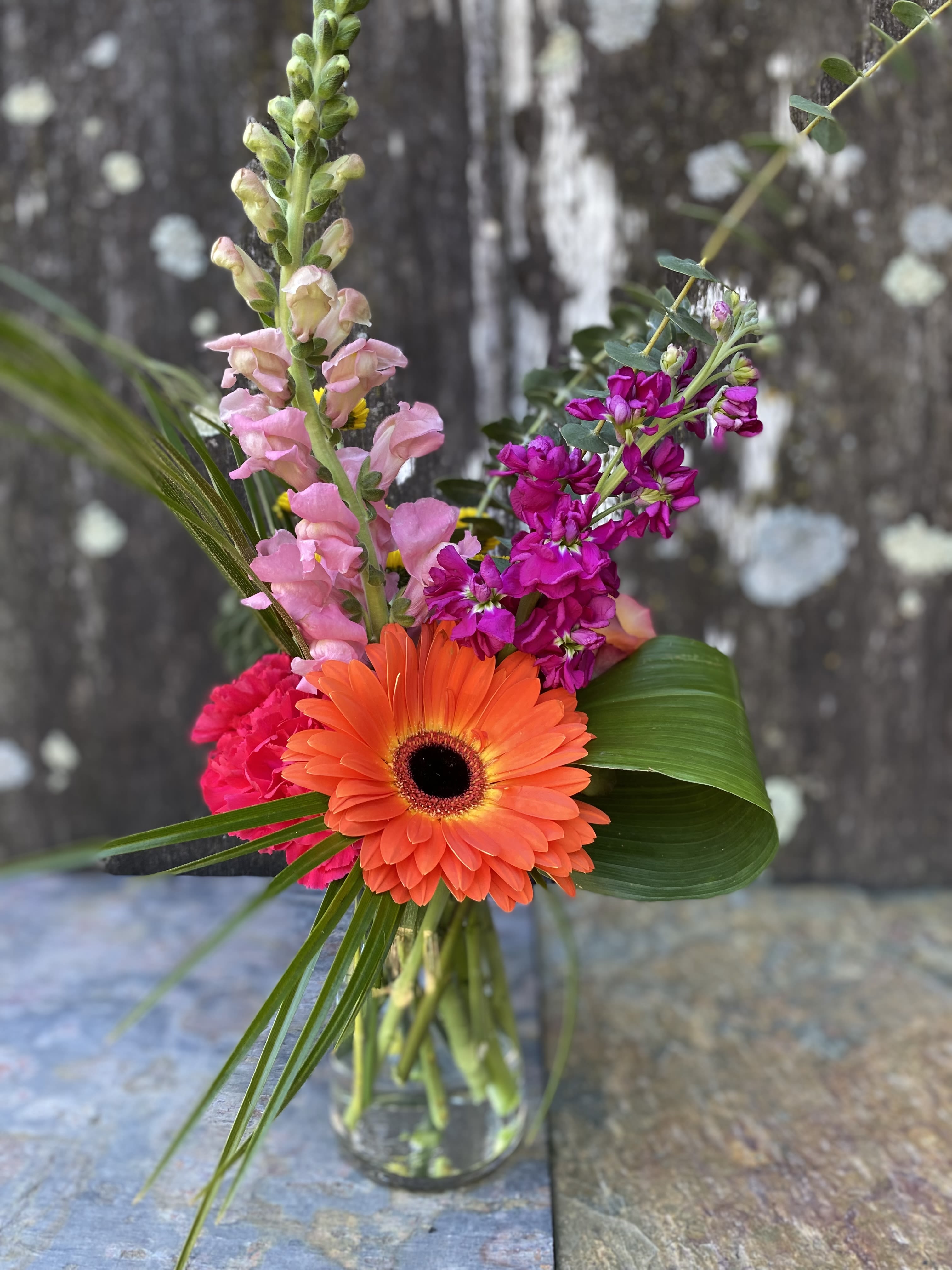 Mixed bouquet with an orange gerbera daisy and pink snapdragons in a glass vase